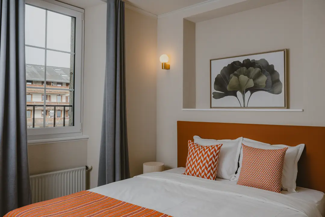 Chambre Deluxe : le lit, coussins orange et estampe au ginkgo