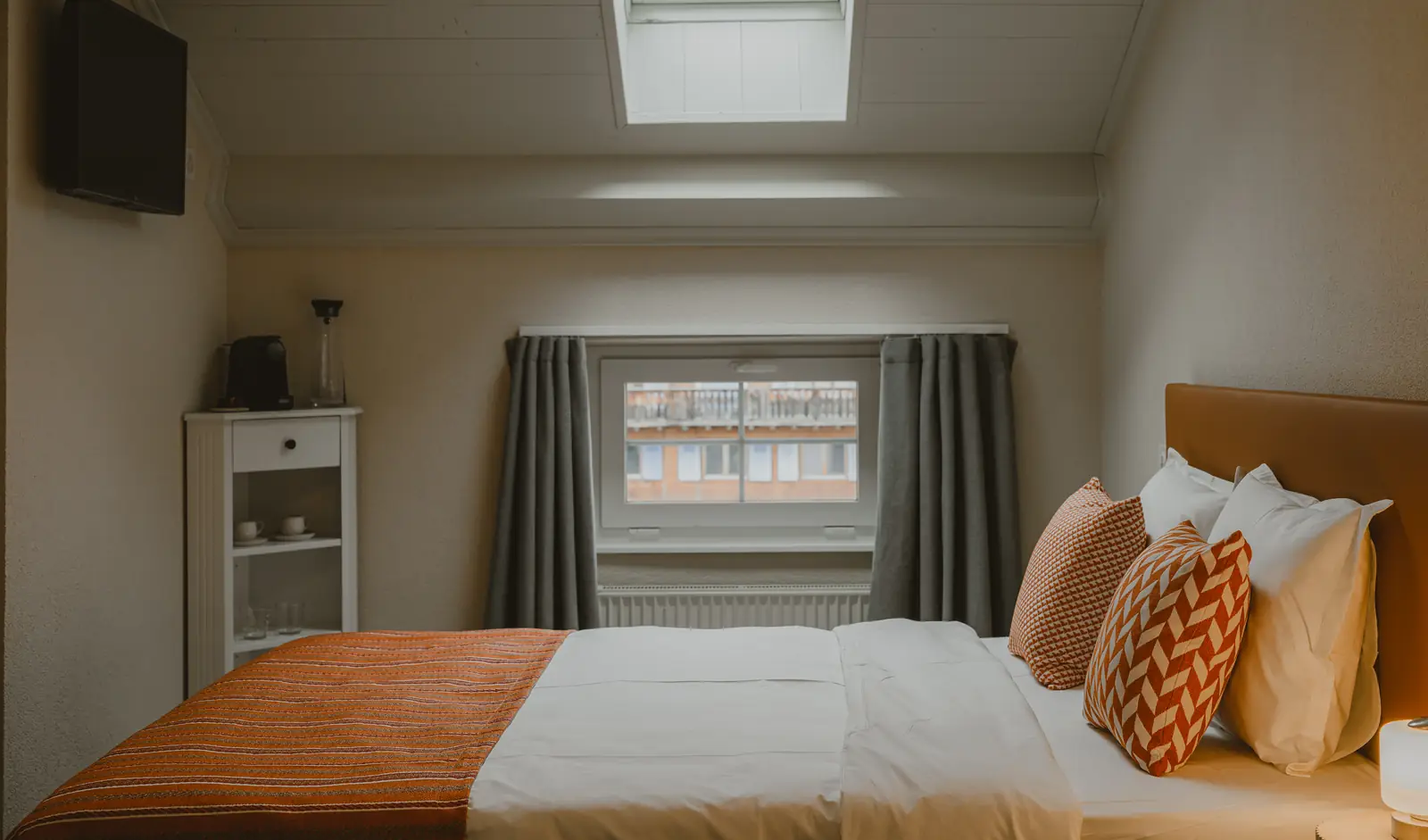 La Chambre Village, sous le toit : le lit, la fenêtre sur le village et le velux